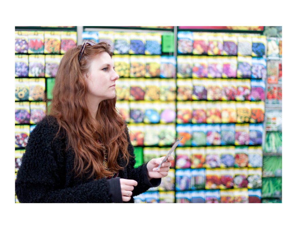 woman trying to decide what seed companies are best while looking at a rack of seeds with seed packet racks behind her